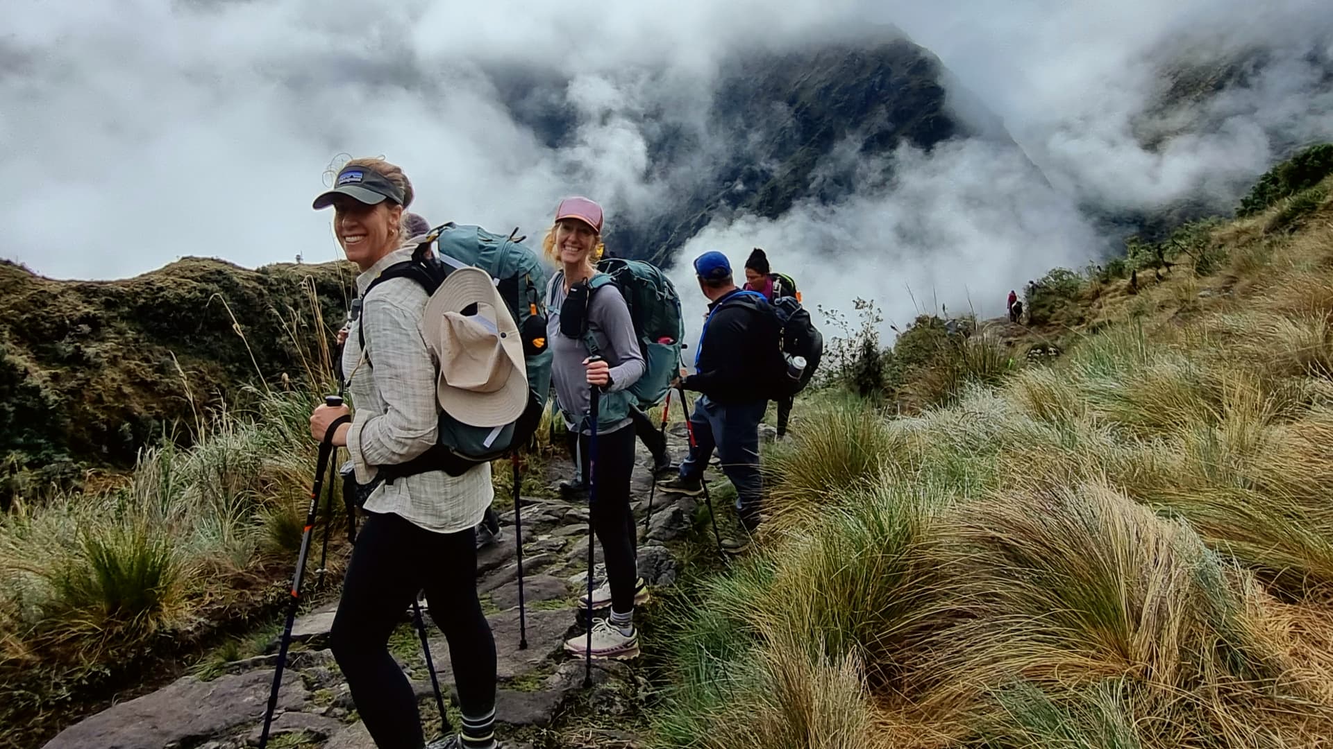 A group of tourists trekking along a scenic trail in the Sacred Valley of the Incas, with terraced fields and towering mountains in the background. A group of tourists trekking along a scenic trail in the Sacred Valley of the Incas, with terraced fields and towering mountains in the background.