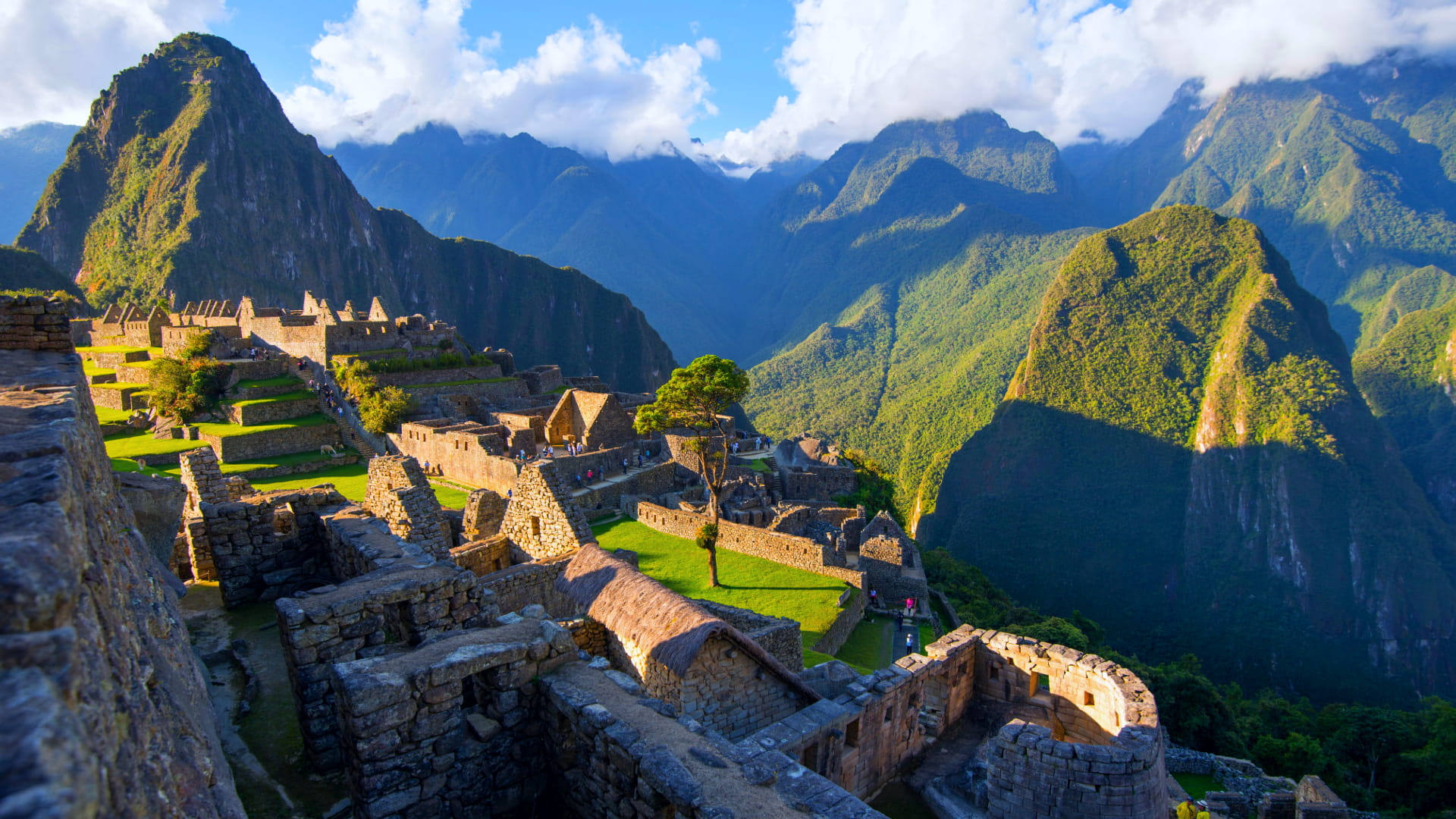 Ancient Inca citadel of Machu Picchu illuminated by morning sunlight, surrounded by lush green mountains under a clear sky.