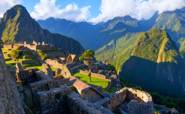 Ancient Inca citadel of Machu Picchu illuminated by morning sunlight, surrounded by lush green mountains under a clear sky.