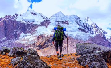 Hiker with a large backpack walking over rocky terrain towards towering snow-covered Andean peaks - Kenko Adventures