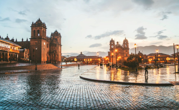 A rainy evening in Cusco’s Plaza de Armas, with reflections on cobblestone streets and illuminated colonial buildings - Kenko Adventures.