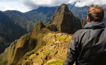 A traveler in a black jacket standing on a viewpoint, gazing at the ancient Inca citadel of Machu Picchu surrounded by lush mountains - Kenko Adventures