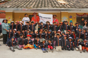 A joyful group of children after a hot chocolate gathering by Kenko Adventures, proudly wearing jackets they received, with the Kenko Adventures banner visible, embodying solidarity and festive cheer.