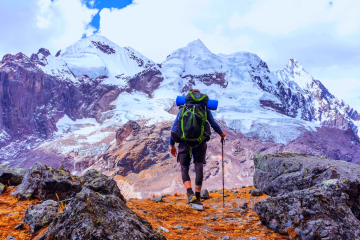 Hiker with a large backpack walking over rocky terrain towards towering snow-covered Andean peaks - Kenko Adventures