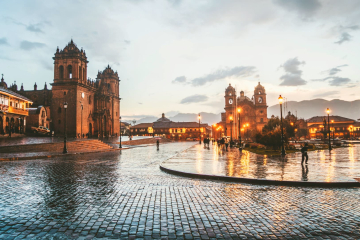 A rainy evening in Cusco’s Plaza de Armas, with reflections on cobblestone streets and illuminated colonial buildings - Kenko Adventures.